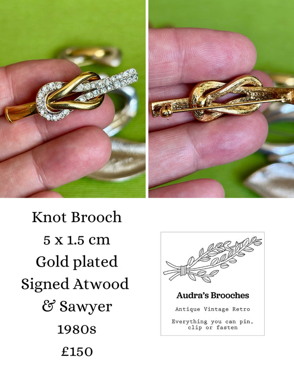 Gold knot brooch held in a hand with product details and Atwood and Sawyer brand logo.