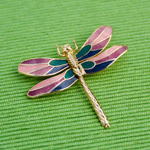 Dragonfly-shaped brooch with purple and green wings on a green textured background