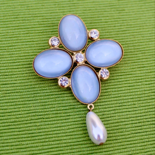 Decorative brooch with blue stones and a pearl on a green textured background