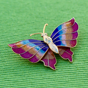 Butterfly-shaped brooch with multicolored wings on a green textured background